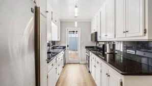A kitchen with white cabinets, a black countertop, and a door leading to a balcony. - Toluca Lake 4BR • Walk to Universal • Yard • Ping Pong (Los Angeles)