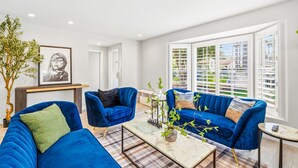 A modern living room with two blue sofas, a coffee table, a plant, and a framed picture on the wall. - Toluca Lake 4BR • Walk to Universal • Yard • Ping Pong (Los Angeles)