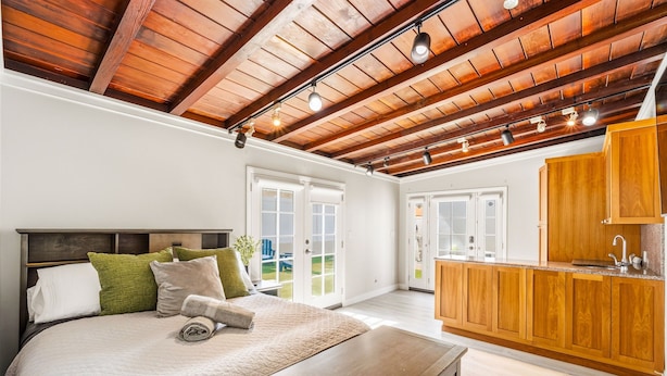 A bedroom with a bed, a wooden ceiling, and a kitchen area with wooden cabinets. - Toluca Lake 4BR • Walk to Universal • Yard • Ping Pong (Los Angeles)
