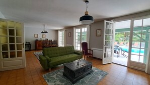 Een ruime woonkamer met een groene bank, een open haard en uitzicht op een zwembad.