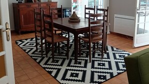 Een eetruimte met een tafel, stoelen, een tapijt met een patroon, een kast en een hanglamp.