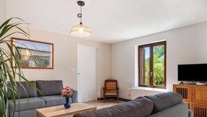Ett vardagsrum med en soffa, en fåtölj, ett soffbord, en tv och ett fönster med utsikt över grönområden.