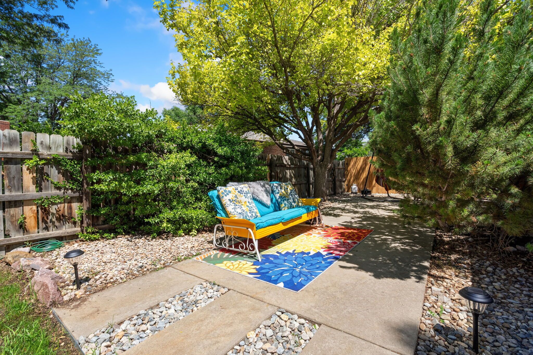 A patio area with a sofa, a colorful rug, and a wooden fence.