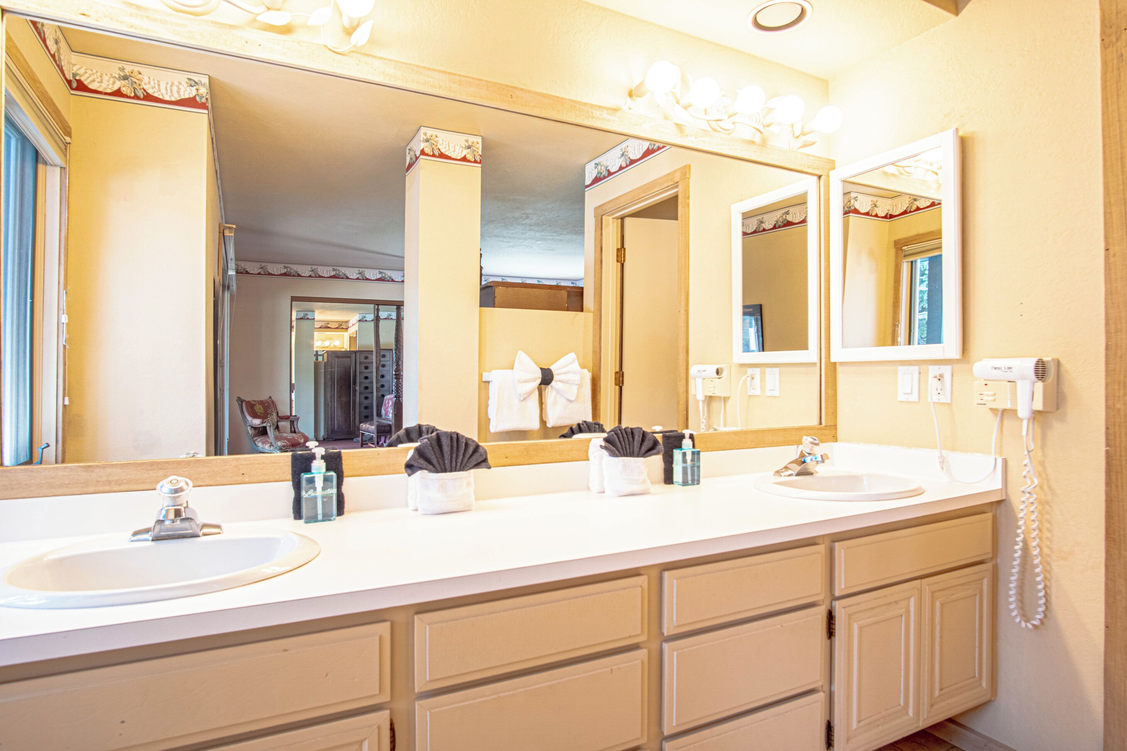 A bathroom with a large mirror, two sinks, and a vanity with drawers.