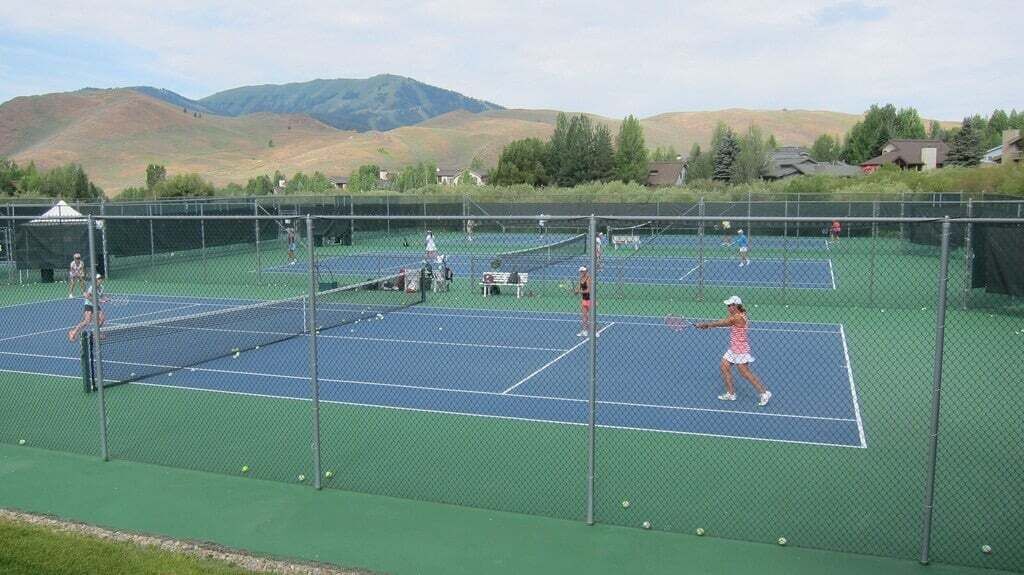 A tennis court with multiple courts, surrounded by a fence, and a mountainous landscape in the background.