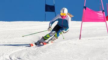 Ein Skifahrer in Bewegung auf einem verschneiten Hang, im Hintergrund wehen Flaggen und ein rosafarbenes Absperrband ist zu sehen.