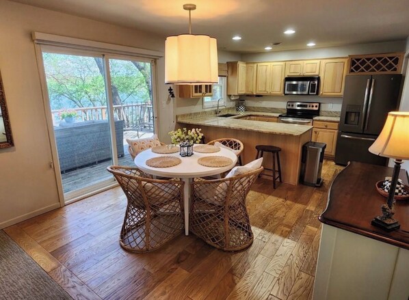 A modern kitchen with wooden cabinets, a central island, and a dining area with wicker chairs.