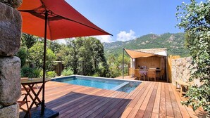 Eine Holzterrasse mit Swimmingpool, einem roten Sonnenschirm und einer Steinmauer.