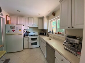 Eine Küche mit weißen Schränken, einem Kühlschrank, einem Backofen, einer Mikrowelle und einer Kaffeemaschine.