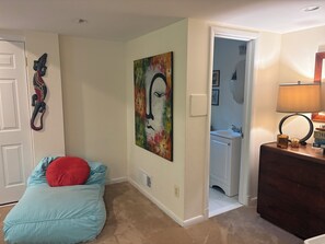 Ein Zimmer mit blauem Sitzsack, einem Bild an der Wand, einer Holzkommode und einer Tür zu einem Badezimmer.