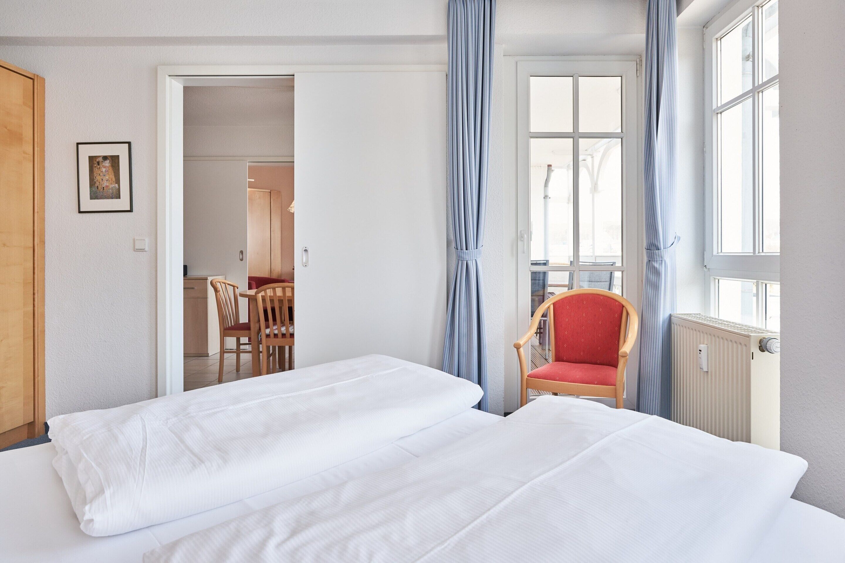 Une chambre d’hôtel avec deux lits, une chaise rouge, une porte en bois et une vue sur l’extérieur.