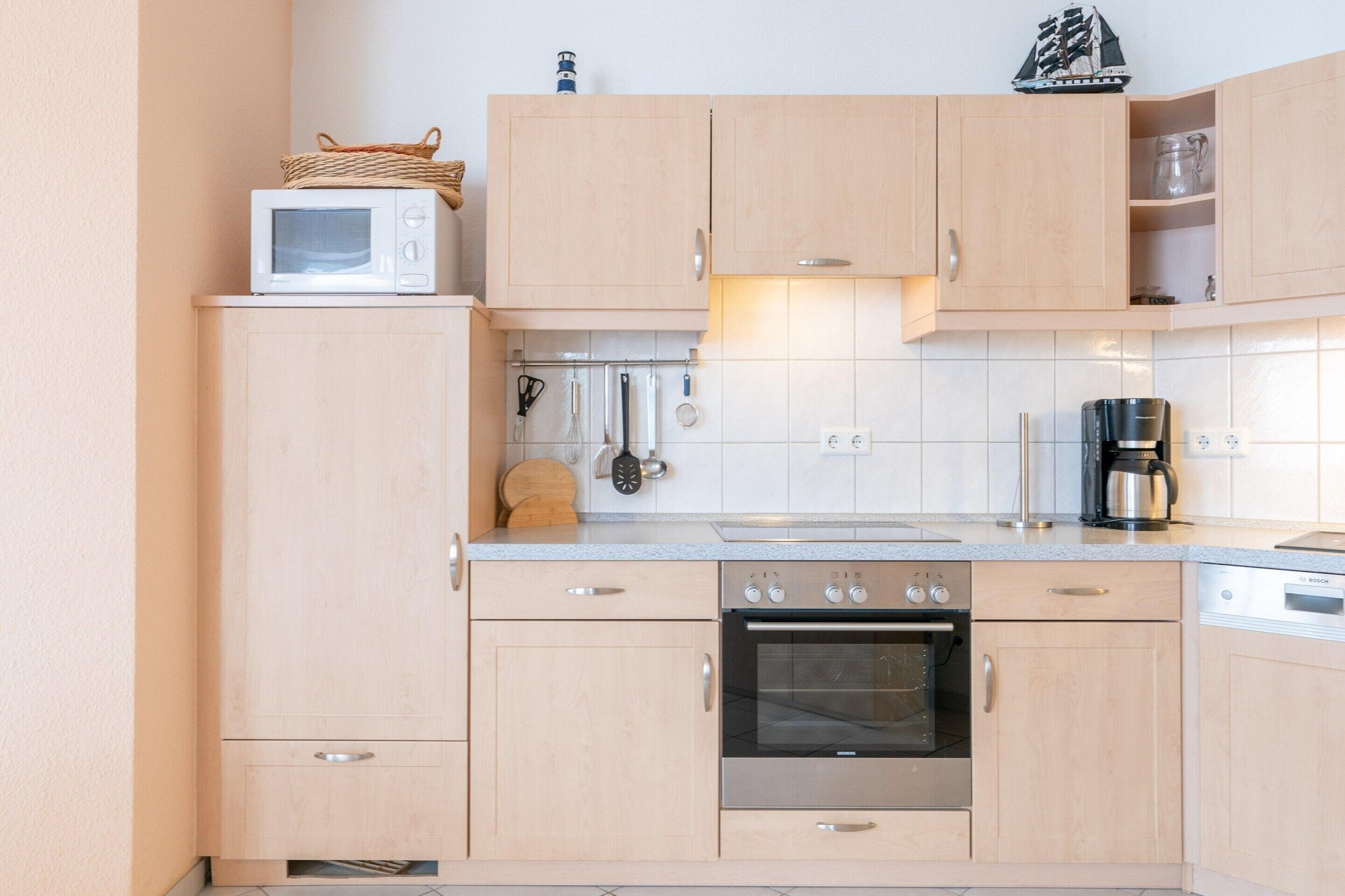Eine kompakte Küche mit Holzausstattung, einer Mikrowelle, einem Backofen und einer Kaffeemaschine.