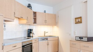 Eine kompakte Küche mit Holzausstattung, einem Geschirrspüler von Bosch, einer Kaffeemaschine und einem Radio.