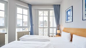 Ein Hotelzimmer mit zwei Betten, großen Fenstern, einem hölzernen Kopfteil und gerahmten Bildern an der Wand.