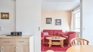 Ein Zimmer mit einem Holztisch, einem roten Sofa, einem Couchtisch aus Holz und einem Esstisch mit Stühlen.
