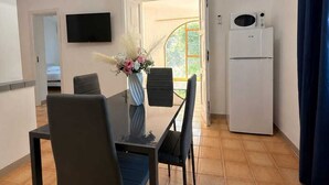 Uma cozinha compacta com mesa, cadeiras, geladeira e TV na parede.