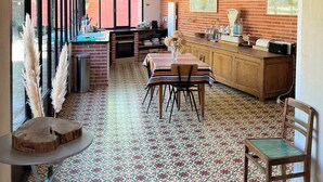 A kitchen with a brick wall, a wooden table, chairs, a clock, and a map.