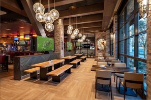 Un restaurant avec des tables et des bancs en bois, des luminaires sphériques suspendus et de grandes fenêtres.