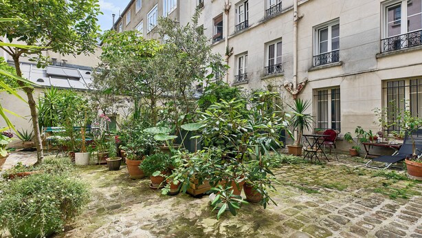 A courtyard with potted plants, a brick floor, and a building with multiple windows and balconies. - Richard Lenoir · 11th · Premium Rooftop Studio – managed by Mey Agency (Paris)