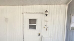 A white door with a window, a small step leading to the door, a potted plant, a metal chair, and a small table. - Cozy Duplex 2 Private 1BR/1BA Suites Sleeps 4 (Inverness)