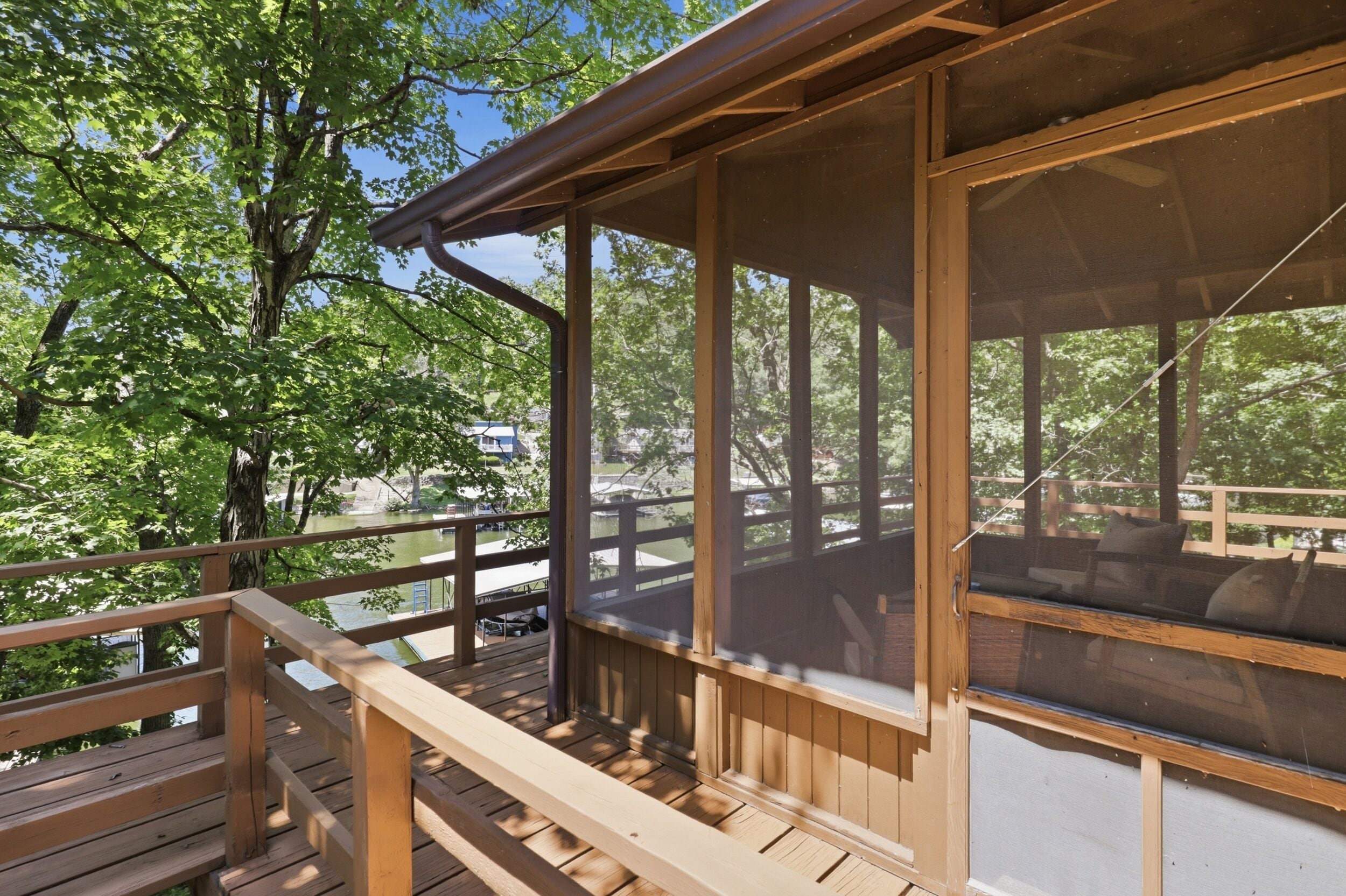 A wooden deck with a railing, overlooking a body of water and trees.