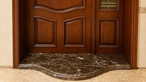 Una porta doppia in legno con il numero '2' sopra, un vetro con motivo geometrico e un piccolo scalino che conduce all'ingresso.