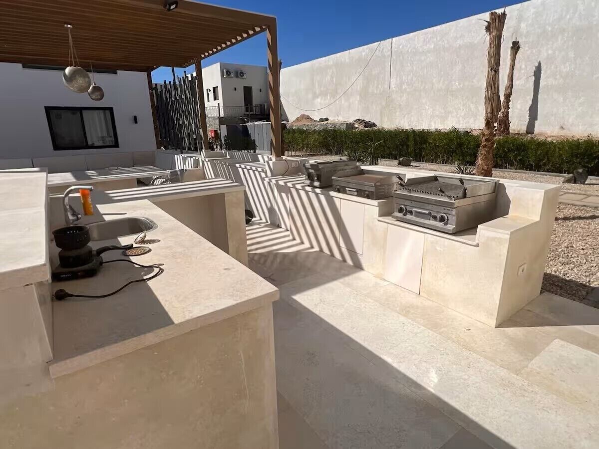 An outdoor kitchen area with built-in seating, a grill, and a wooden pergola.