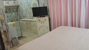 Un dormitorio con una cama, un aparador, un televisor encima y una cortina.