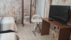 Un dormitorio con cama, escritorio con televisor, silla y retrete.