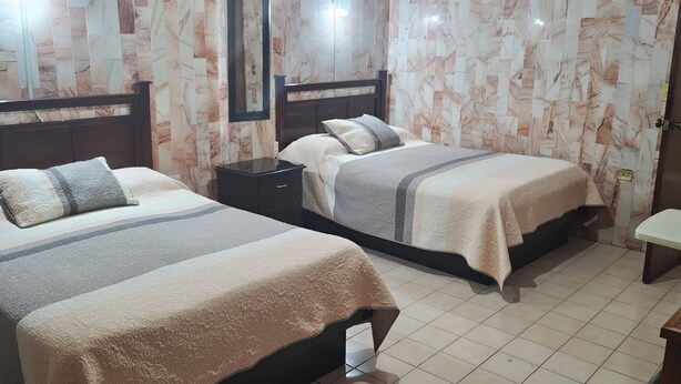 Habitación de hotel con dos camas, una mesita de noche, un espejo y una puerta.
