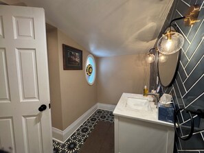 A bathroom with a white door, a framed picture, a stained glass window, a sink with a mirror, and a patterned floor. - Spacious 4-bedroom house in charming Denver with central air cooling (Denver)