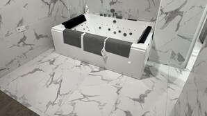 Un baño moderno con suelo de mármol, una bañera y un espejo grande.