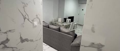 Un interior moderno con paredes y suelo de mármol, un sofá gris, y un comedor con sillas y una mesa.