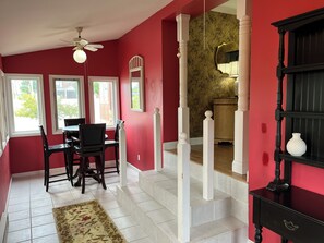 Ein Zimmer mit Esstisch und Stühlen, einer Treppe und einem schwarzen Schrank mit weißer Vase.