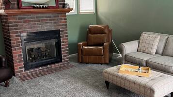 Un salon avec une cheminée en briques, un fauteuil en cuir, un canapé et un ventilateur de plafond.