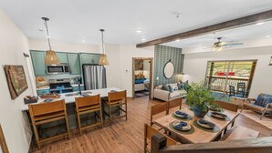 Eine moderne Küche mit Holdekor, eine Essecke mit einem Holztisch und -stühlen sowie ein Wohnzimmer mit einer Couch und einem großen Fenster.