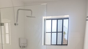 Una dutxa envidrada amb finestra, un vàter blanc i una presa elèctrica a la vista.
