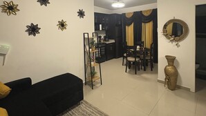 A living room with a black sofa, a coffee table, decorative wall art, a dining area with chairs, a kitchen in the background, and a ceiling light fixture. - La nueva San Migue is a  safe place ,w 2  bedrooms, pool ,restaurants near, (San Miguel)