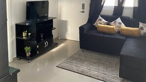 A living room with a flat-screen TV, black entertainment unit, dark sofa with yellow cushions, and a patterned rug. - La nueva San Migue is a  safe place ,w 2  bedrooms, pool ,restaurants near, (San Miguel)