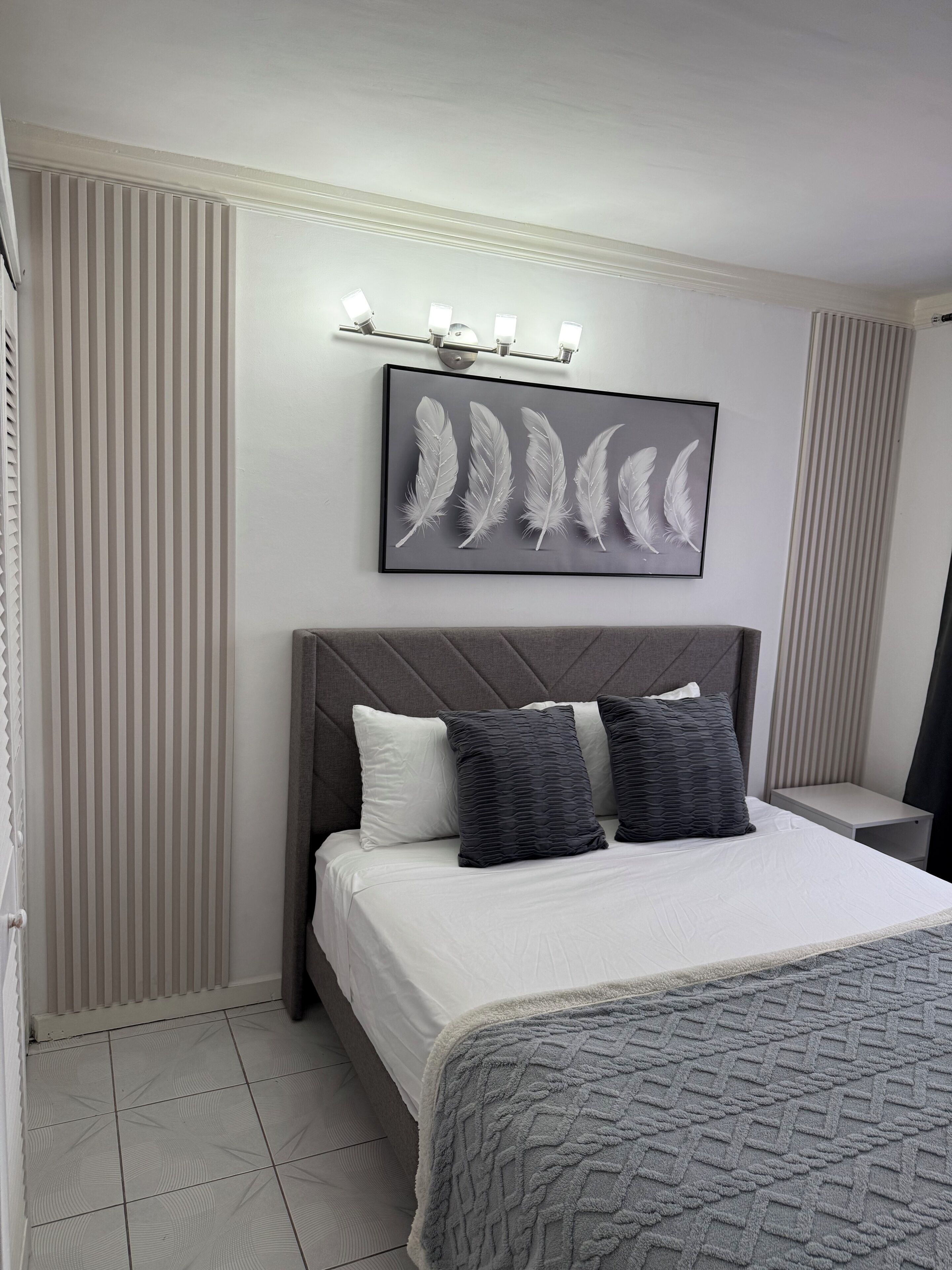 Hotelkamer met een bed, hoofdeinde, nachtkastje, wandlamp en een kunstwerk in een lijst.