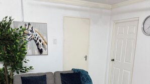 Olohuoneessa on harmaa sohva, pyöreä puinen pöytä, kattotuuletin, seinälle kiinnitetty kello ja kirahvin kuva.