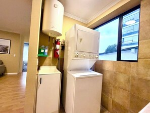 Eine kompakte Küche mit Waschmaschine und Trockner, einem Feuerlöscher und einem Fenster mit Blick auf ein Gebäude.