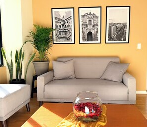 Ein Wohnzimmer mit einer Couch, einer Glasvase mit Blumen und drei gerahmten Schwarz-Weiß-Fotos an der Wand.