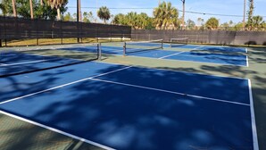 Una cancha de tenis con una red, rodeada por una cerca y árboles.