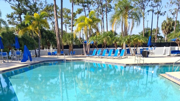 Una piscina cristalina con sillones reclinables azules y una valla blanca al fondo.