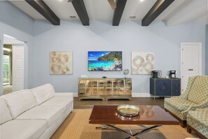 Ein Wohnzimmer mit einem weißen Sofa, einem Glastisch und einem Bild von einer Strandlandschaft.