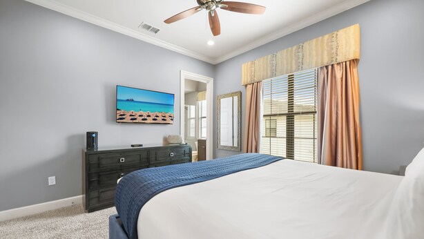 Quarto com cama, ventoinha no teto, cômoda, televisão e janela com cortinas.