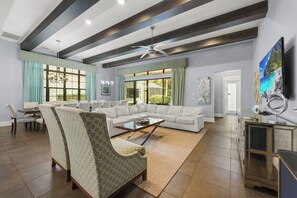 A spacious living room with a large sectional sofa, a dining area with a table and chairs, and a television mounted on the wall. - Enchanted Estate at Reunion | 9BR Stay w/ Arcades, Theater, and Private pool (Kissimmee)