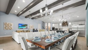 Uma área de jantar moderna com uma mesa de madeira comprida posta para seis pessoas, rodeada por cadeiras estofadas brancas.