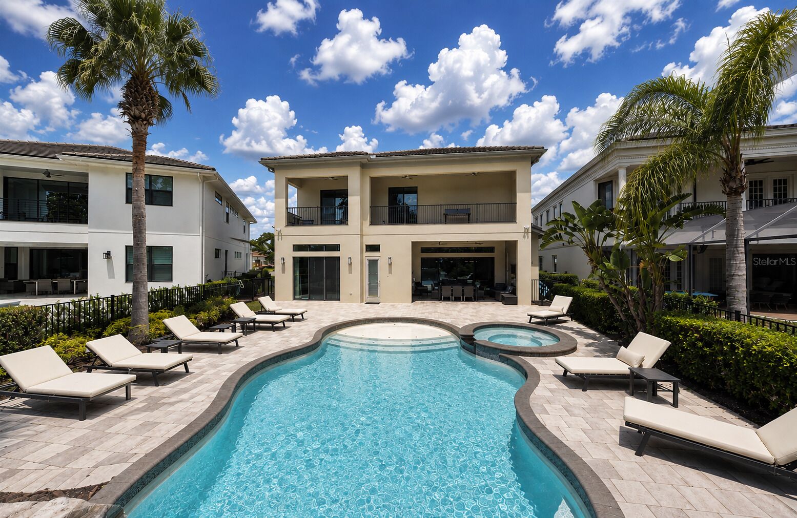 A swimming pool with lounge chairs, a two-story building, and palm trees.